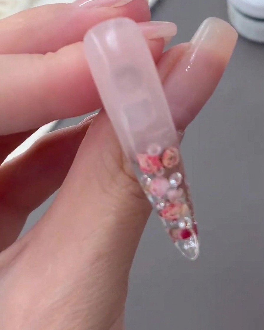 Una tip trasparente polimerizzata sollevata per mostrare il design floreale incapsulato e lo sfondo con gradiente lattiginoso.