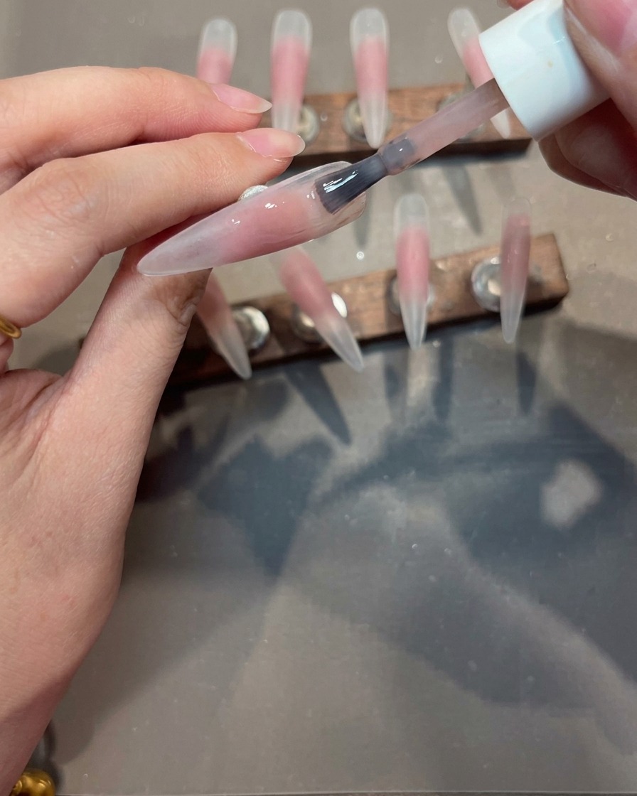 Pennello che stende uno strato di gel nude su una tip con centro rosa.