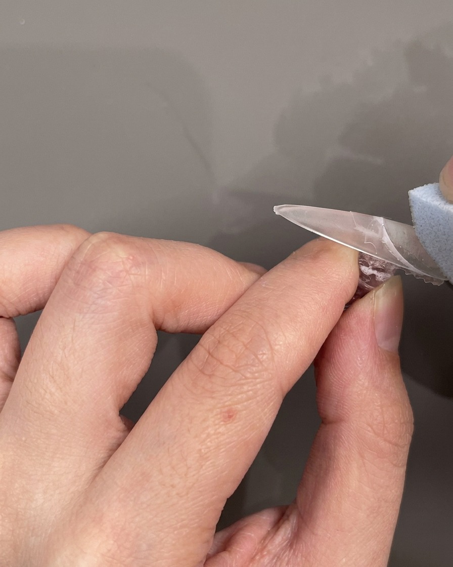 Un adesivo in silicone per linea del sorriso French posizionato orizzontalmente sullunghia.