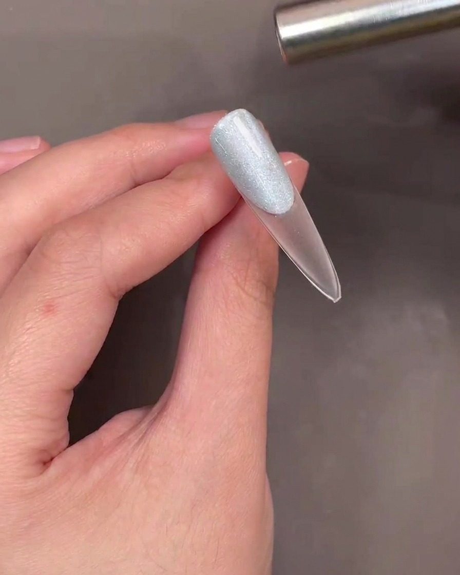 Un bastoncino magnetico tenuto sopra ununghia con gel cat-eye blu per creare leffetto shimmer.