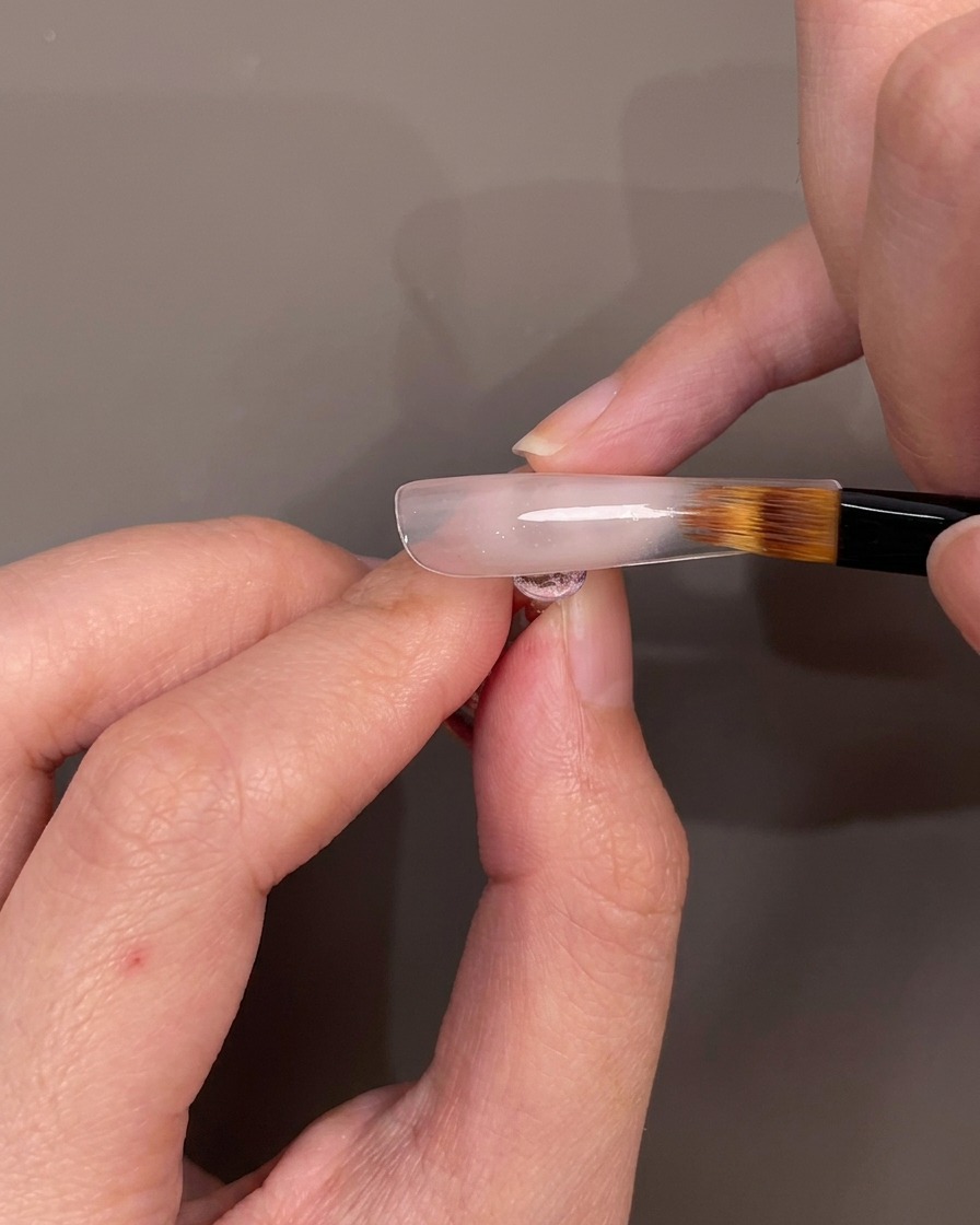 Un pennello sfuma lo smalto gel nude verso il basso su una punta per creare un effetto ombré.