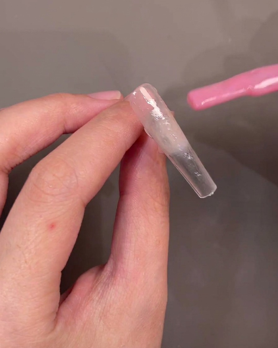Un pennello applica smalto gel rosa traslucido diagonalmente attraverso la punta.