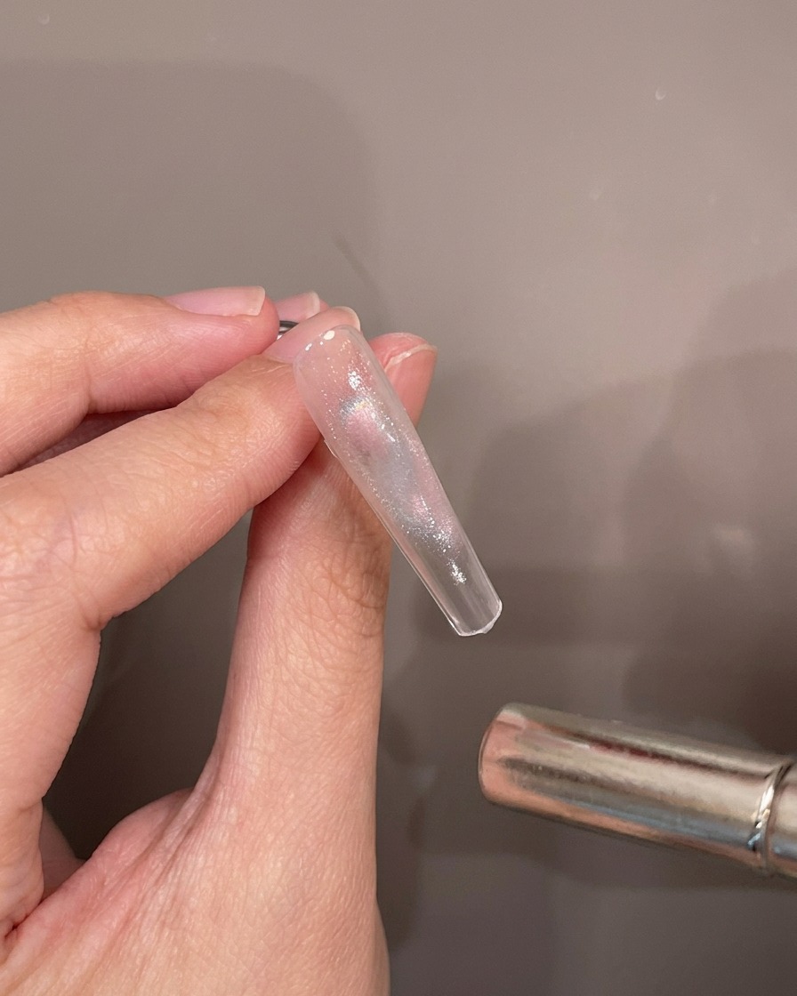 Una mano che tiene una tip trasparente mentre un magnete cilindrico passa sopra il gel cat-eye umido.