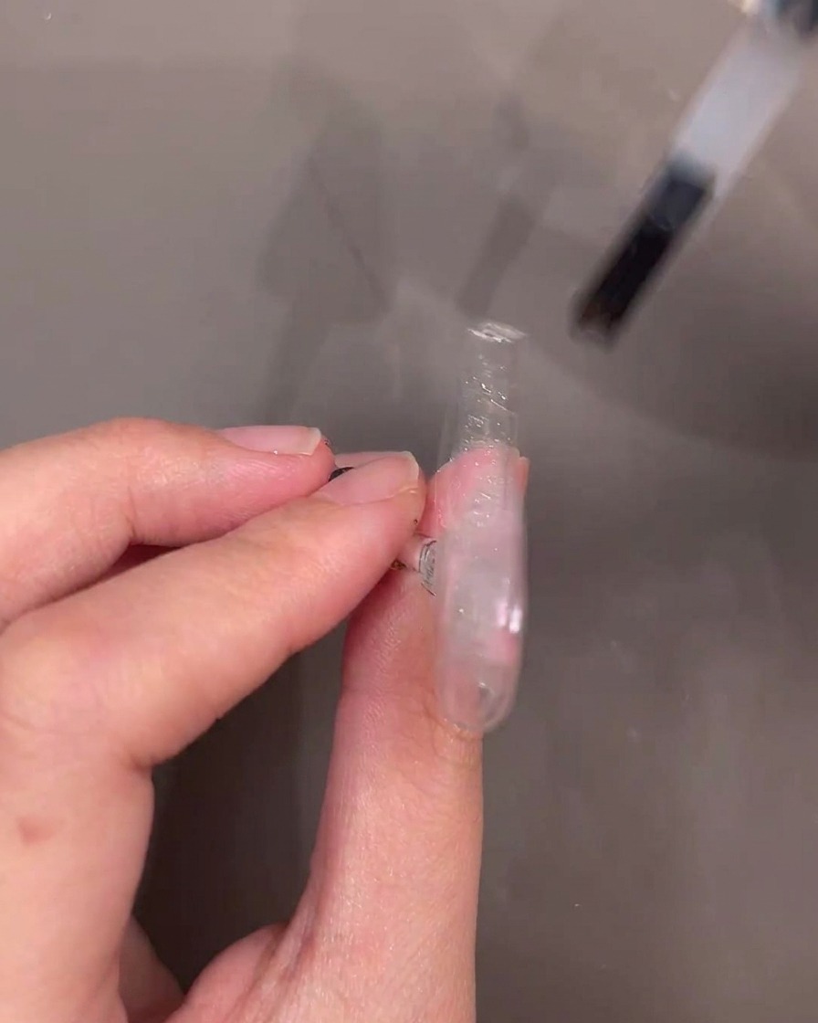 Il pennello di un flacone di gel applica uno strato di gel di rinforzo trasparente su una punta decorata.