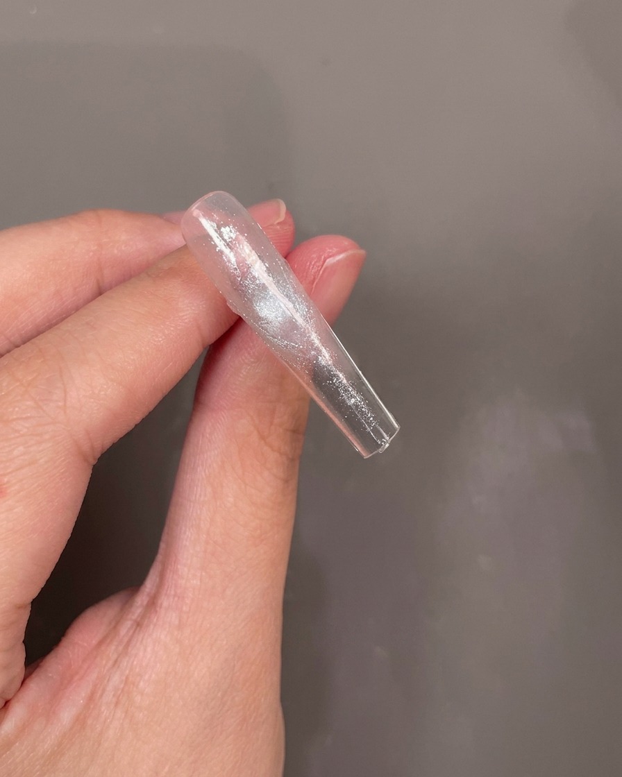 Il retro di una tip trasparente con un piccolo fiore secco blu posizionato con cura in uno strato di gel umido.