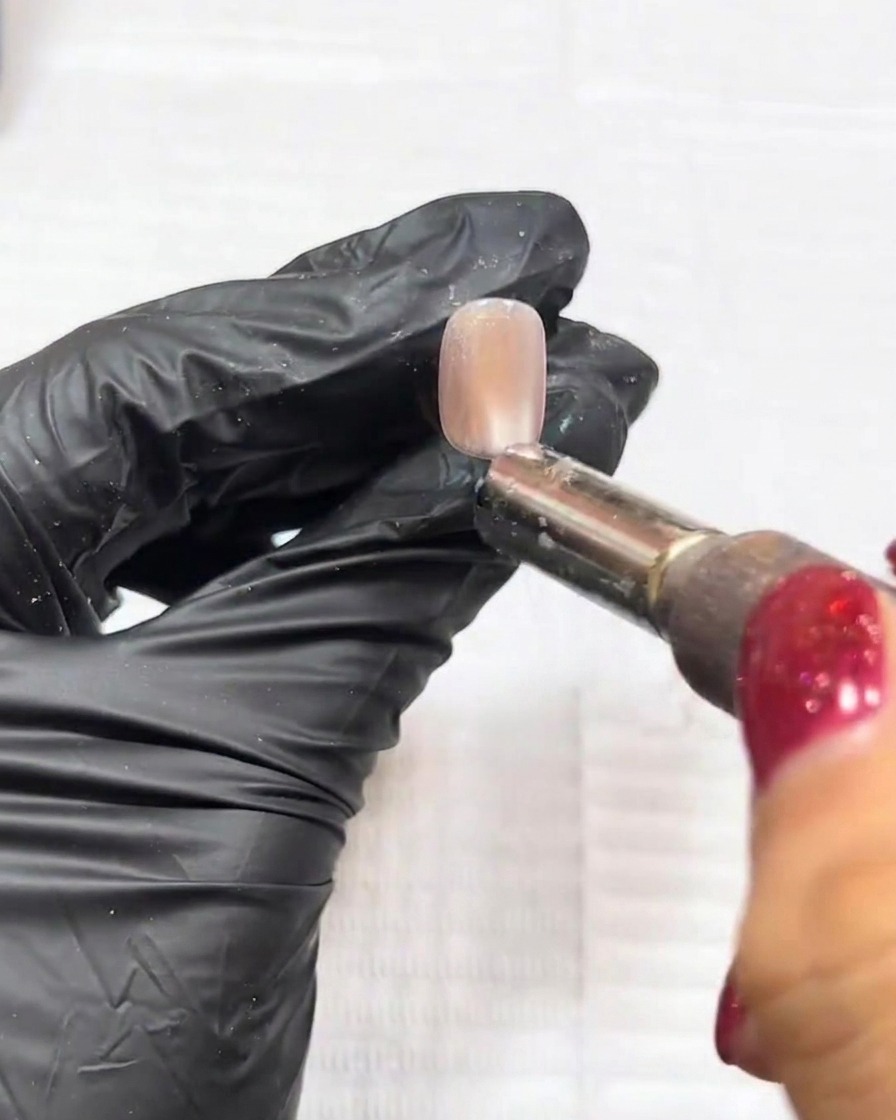 Scatto ravvicinato che mostra un magnete utilizzato sopra ununghia per manipolare le particelle cat-eye in un riflesso centrale definito.