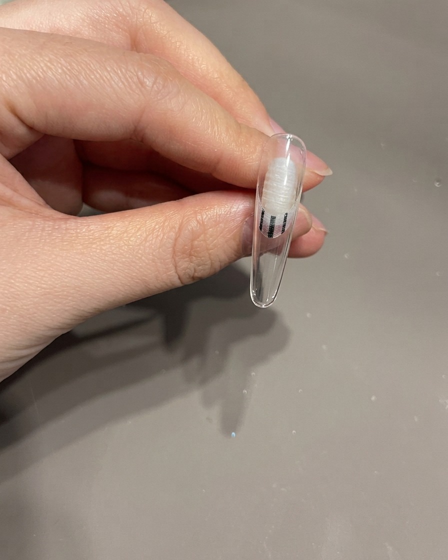 Primo piano di una mano che posiziona ununghia con un fiocco 3D sotto una lampada UV per la polimerizzazione.