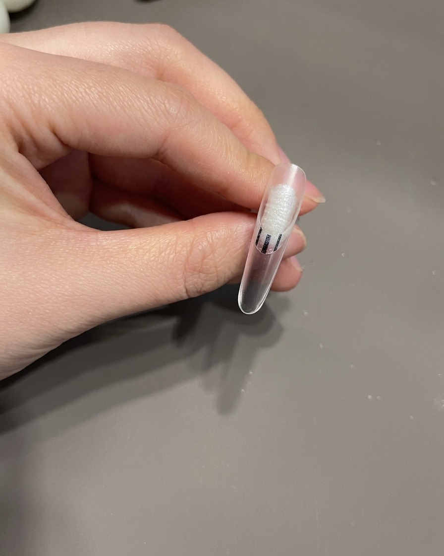 Un pennello di precisione che disegna sottili linee bianche con un motivo a vortice su ununghia rivestita di gel.