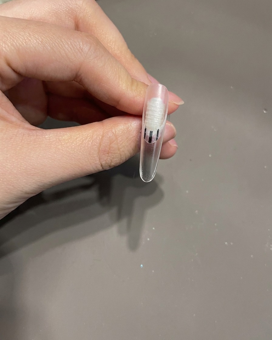 Un pennello da unghie che applica una piccola goccia di top coat trasparente sulla superficie dellunghia come colla per un abbellimento.