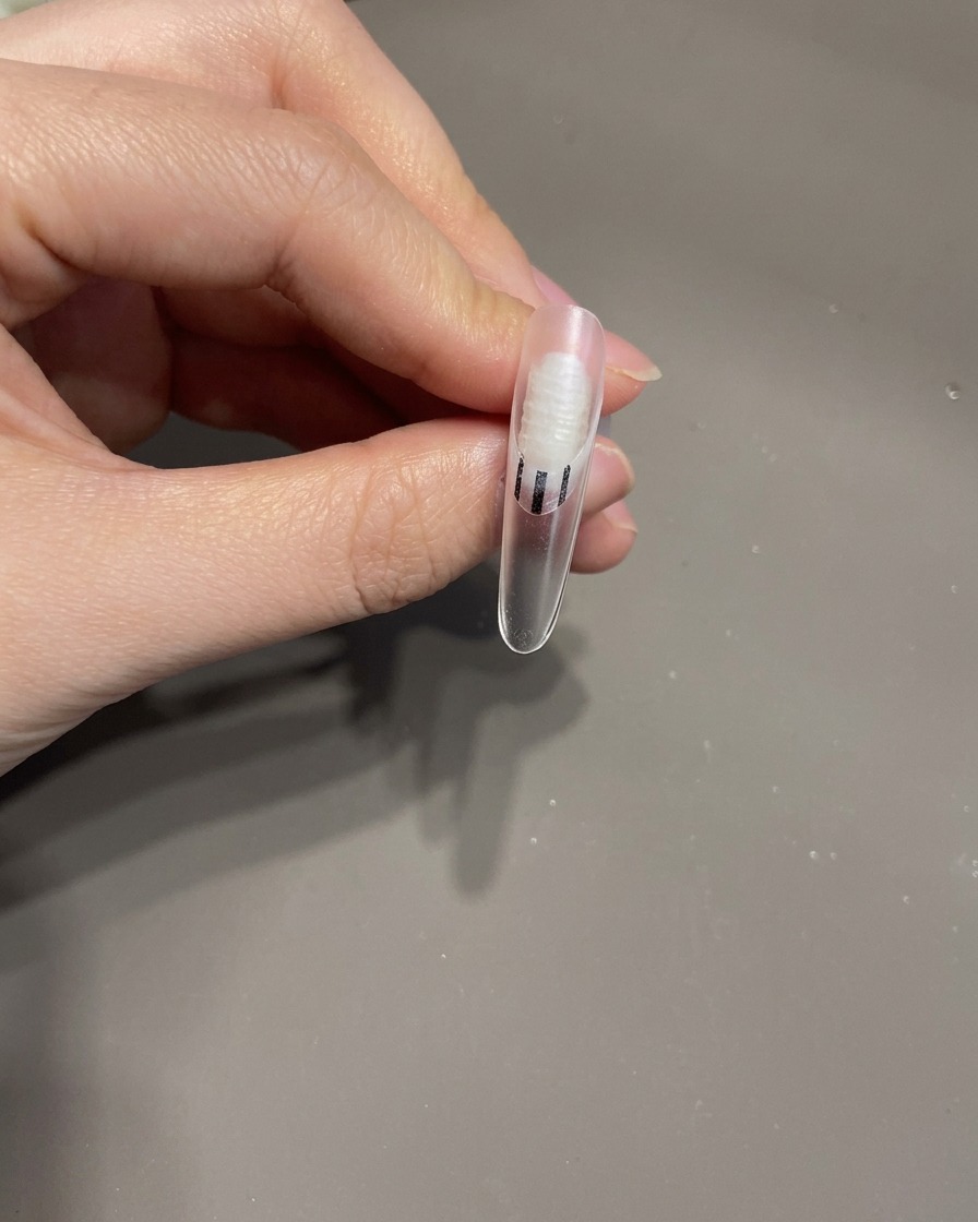 Pinzette che posizionano un piccolo fiocco 3D in gel sulla superficie di ununghia curata.