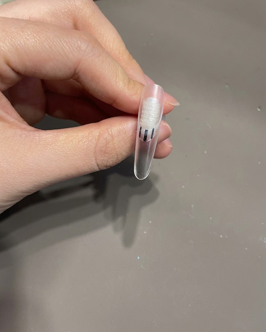 Ununghia finita con un fiocco 3D e linee bianche sinuose allinterno di una lampada UV per il processo di polimerizzazione finale.