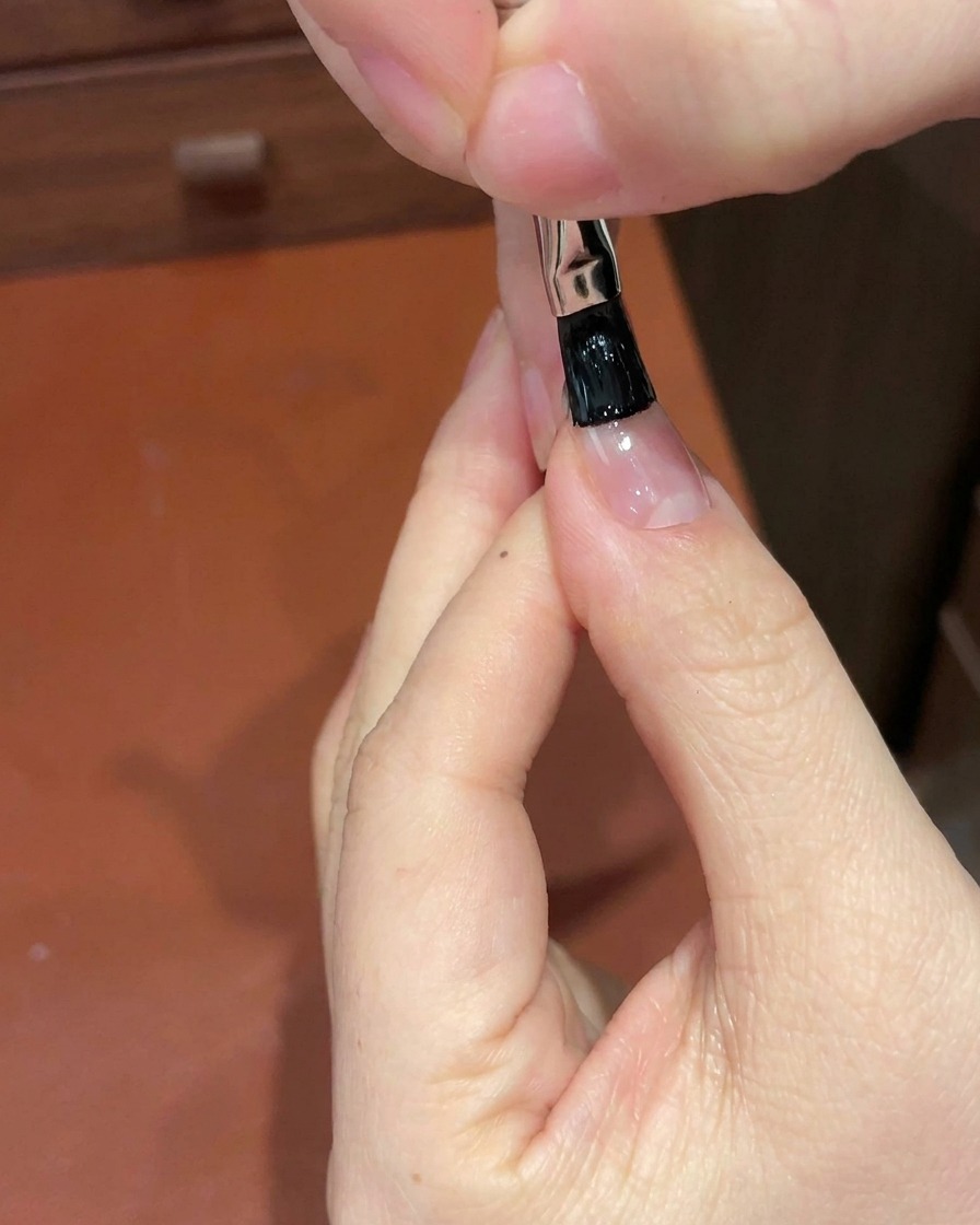 Un pennello a punta sottile applica gel nero sul bordo libero dellunghia.