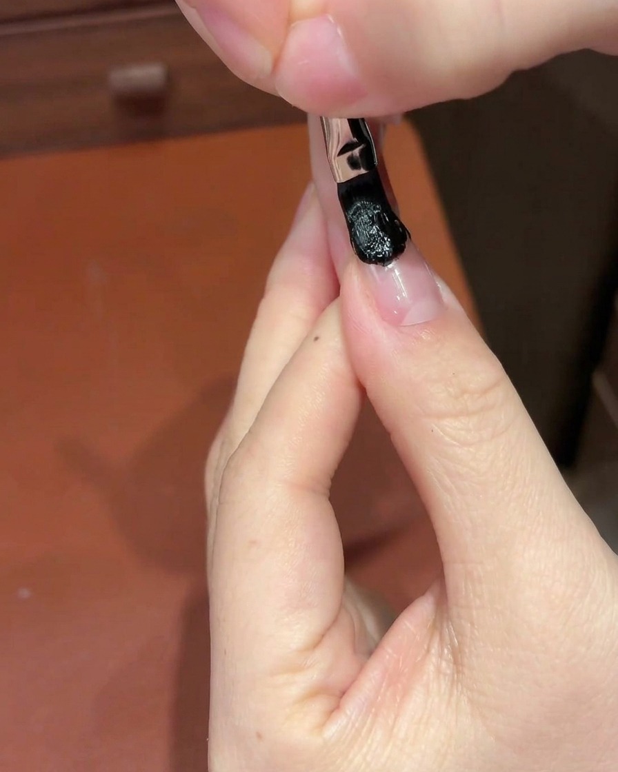 Una spugnetta cosmetica tampona la sezione di gel nero sullunghia per creare un gradiente.
