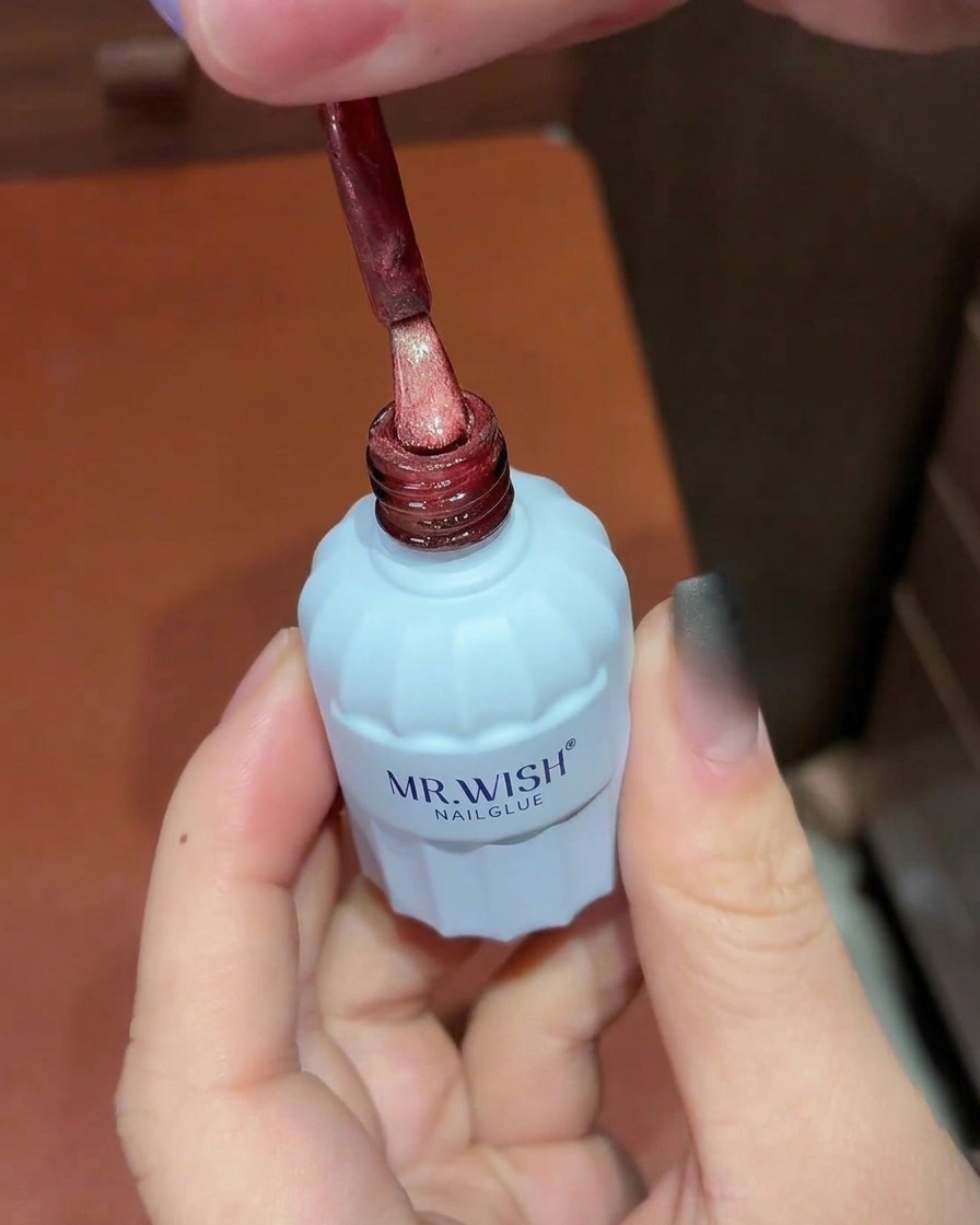 Un pennello applica smalto gel cat-eye rosso brillante sopra ununghia ombré nera.