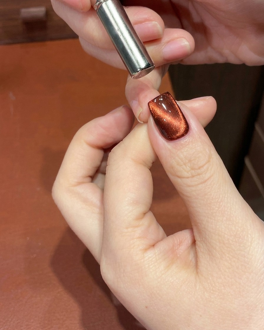 Dettaglio di ununghia gel cat-eye rossa con un magnete vicino alla cuticola che sposta il riflesso in un gradiente profondo.