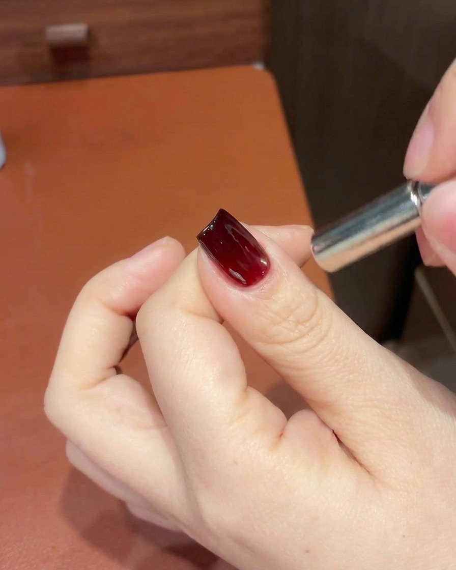 Dettaglio di una mano che tiene un magnete vicino alla punta di ununghia cat-eye rossa per rifinire la posizione del riflesso.