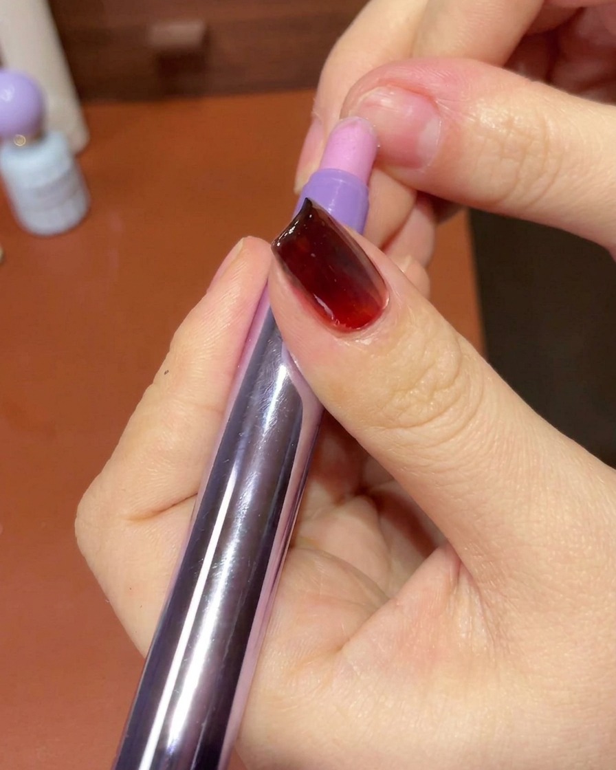 Una mano usa un pad che non lascia pelucchi per pulire la pelle e i bordi attorno a ununghia con gel manicure.