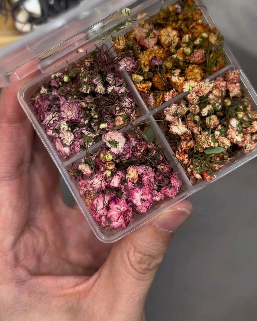 Una pinzetta posiziona con cura un piccolo fiore secco su una tip.