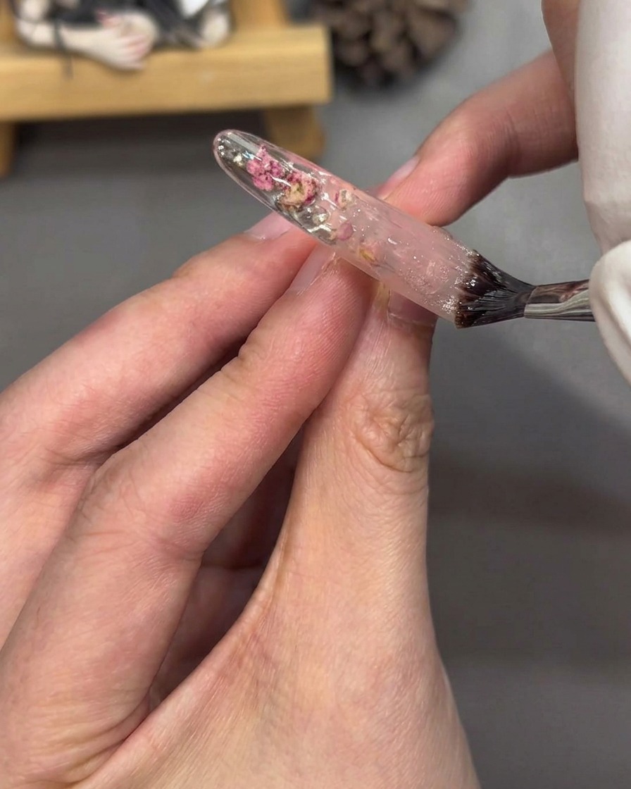 Un pennello applica il top coat trasparente su una tip completamente decorata, creando una finitura lucida.
