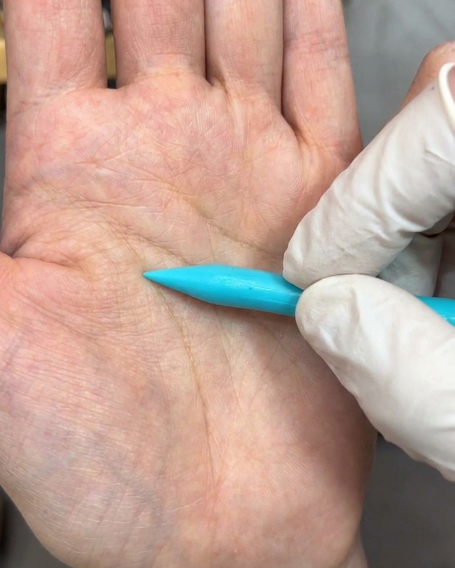 Uno strumento per scultura preme una pallina di gel bianco su una superficie, formando la sagoma di un petalo delicato.