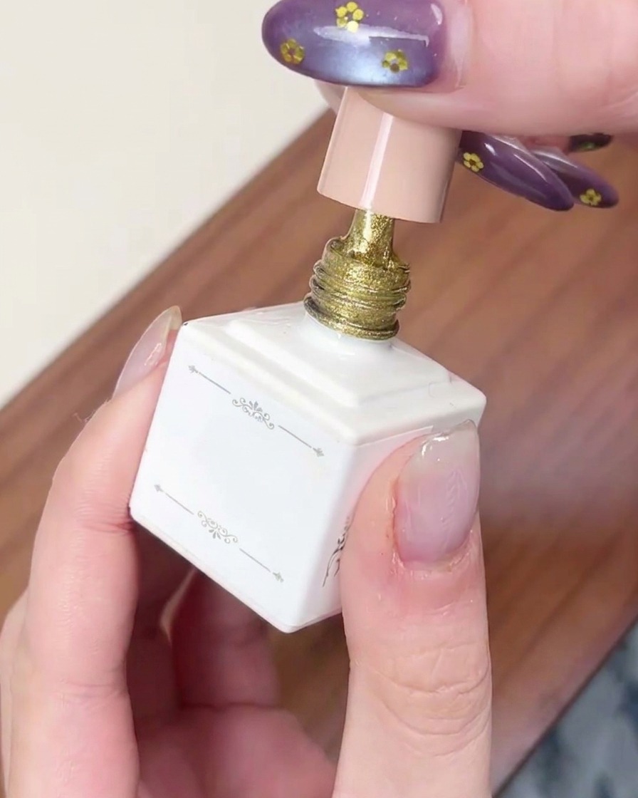 Un pennello applica uno strato di smalto gel cat-eye color oro scintillante su ununghia.