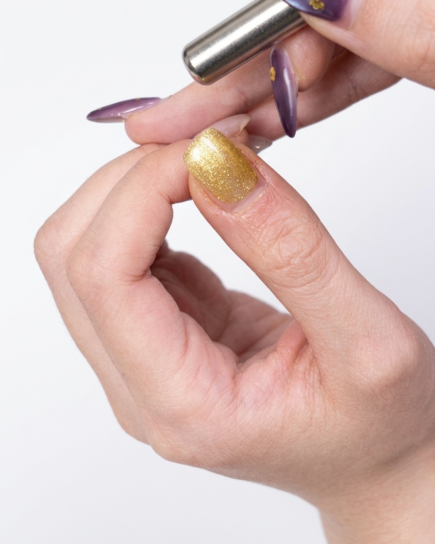 Uno strumento magnetico tenuto vicino al lato di ununghia rivestita di gel oro per spostare le particelle magnetiche.