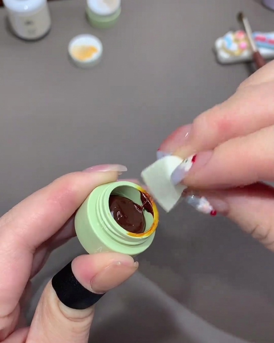 Una mano che usa un piccolo pezzo di spugna per trucco per prelevare gel arancione scuro da un vasetto verde.