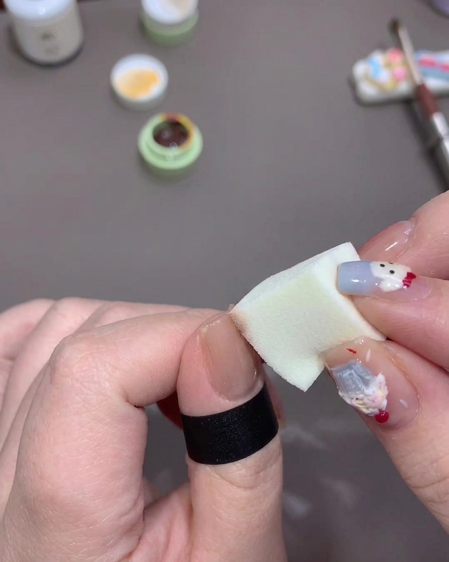 Una mano che picchietta una piccola spugna per trucco carica di gel arancione sulla punta dellunghia del pollice per creare una sfumatura morbida.