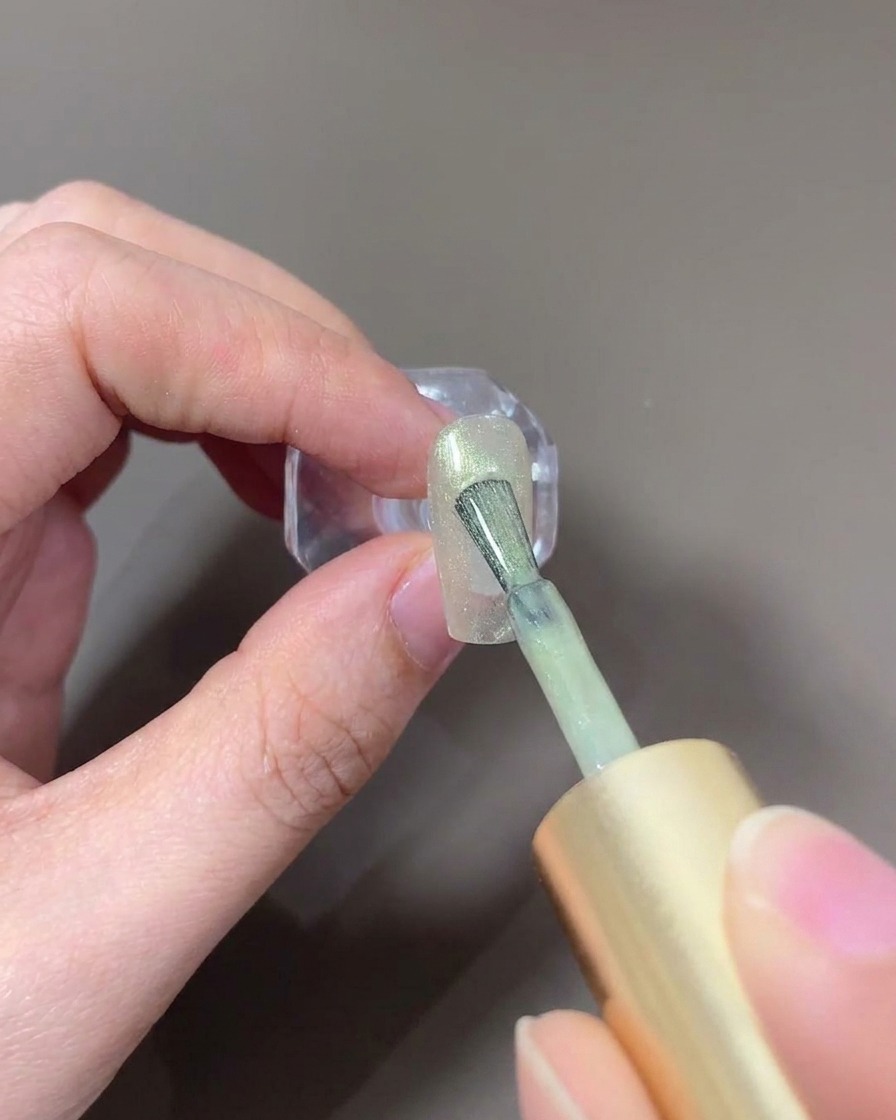 Un pennello per unghie che applica un gel cat-eye vetro di colore chiaro su ununghia.