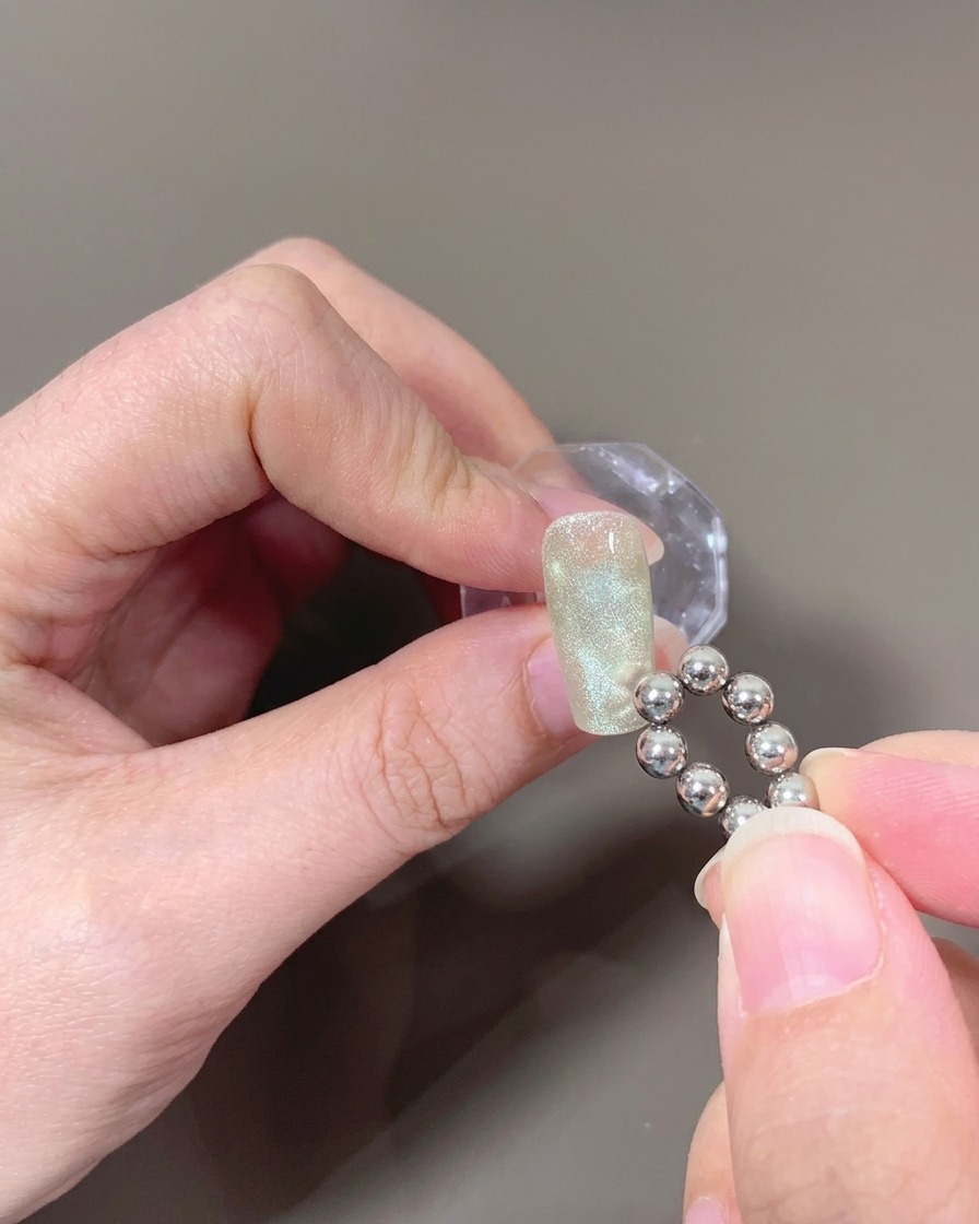 Un primo piano di ununghia con gel cat-eye non polimerizzato, mentre un magnete a sfera crea un motivo a onde.