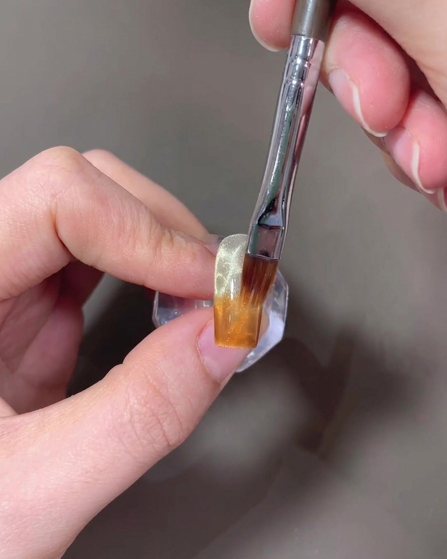Un pennello che sfuma il gel ambra verso lalto su ununghia per creare un gradiente.