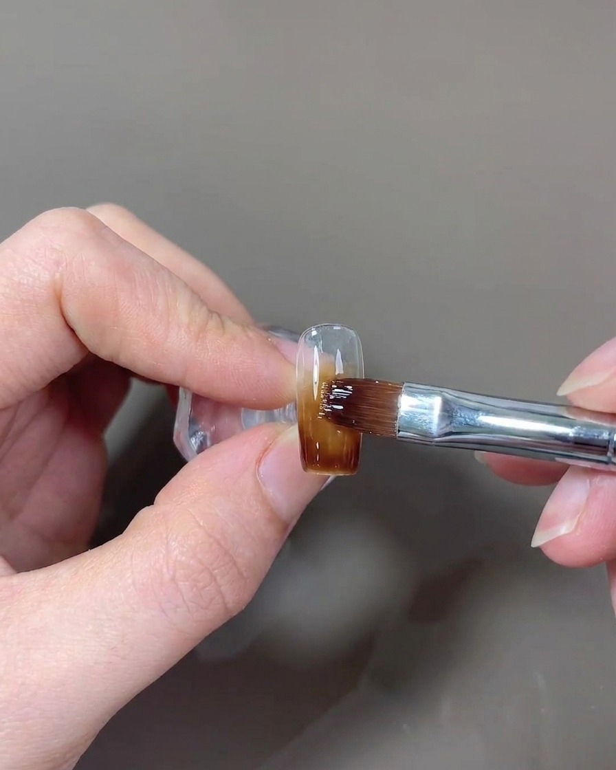 Un pennello che applica uno strato finale di top coat lucido sullunghia.