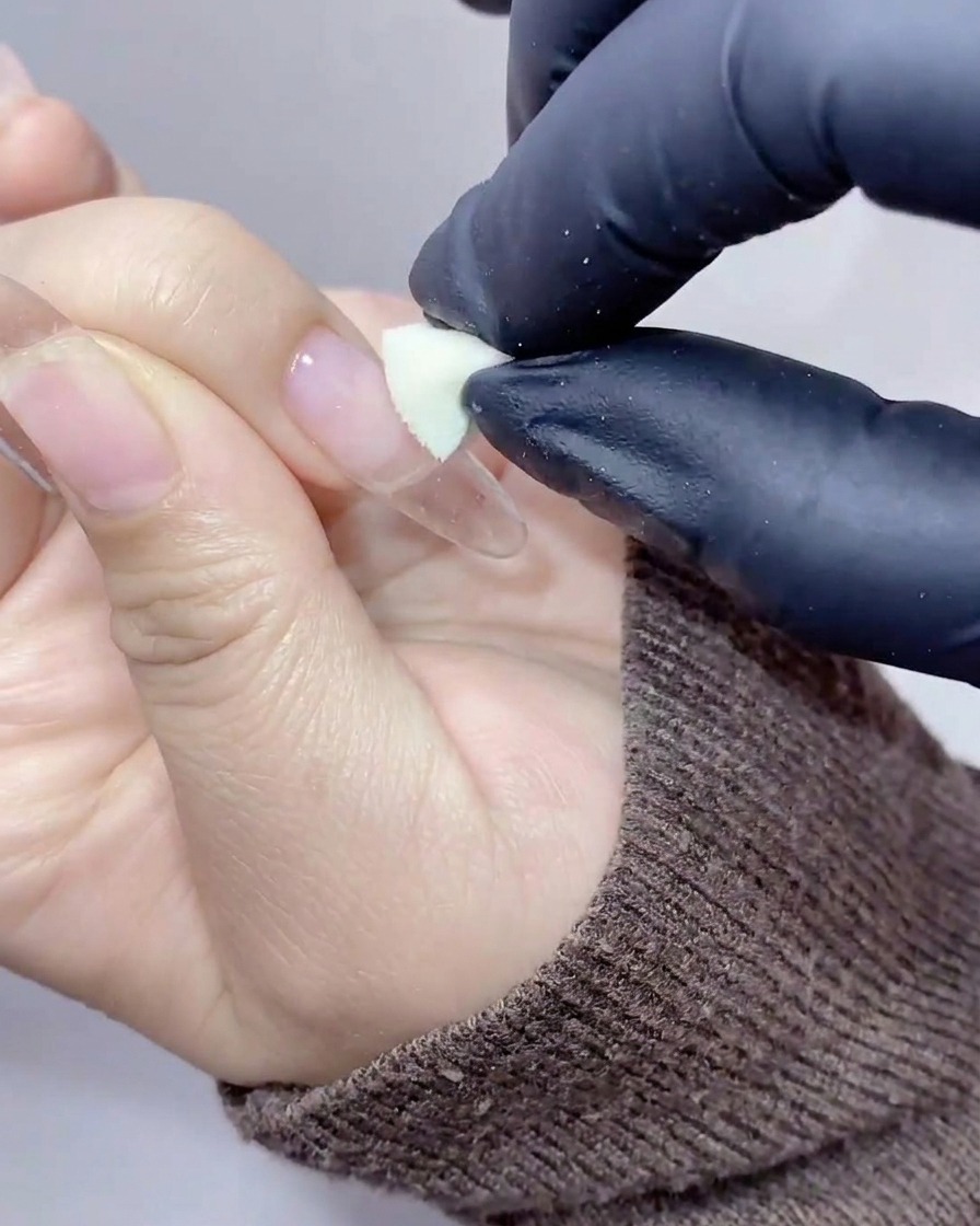Mani con guanti usano una spugnetta cosmetica per picchiettare gel color pesca-arancio al centro dellunghia.