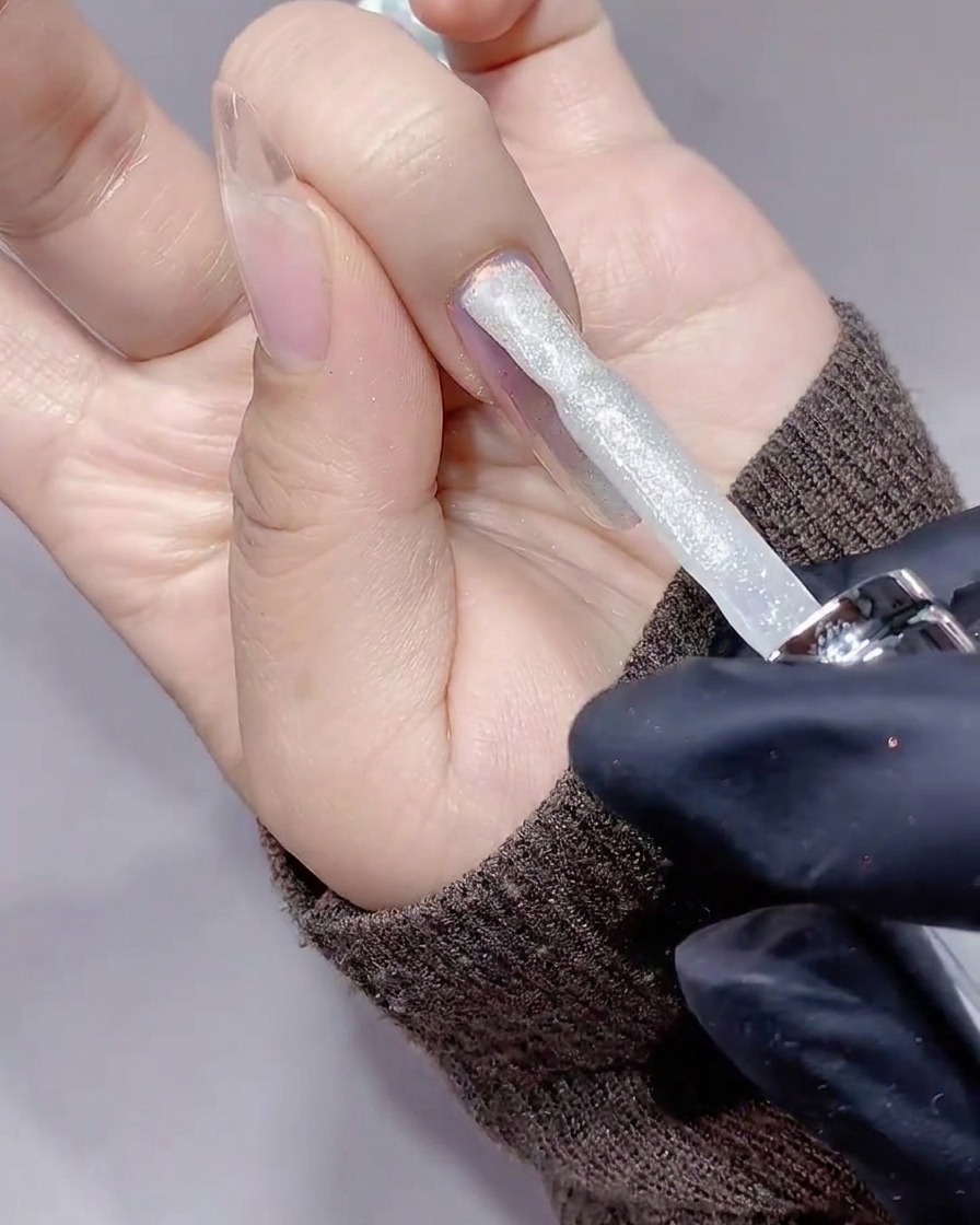 Un pennello che applica un gel glitter argento effetto diamante su ununghia.