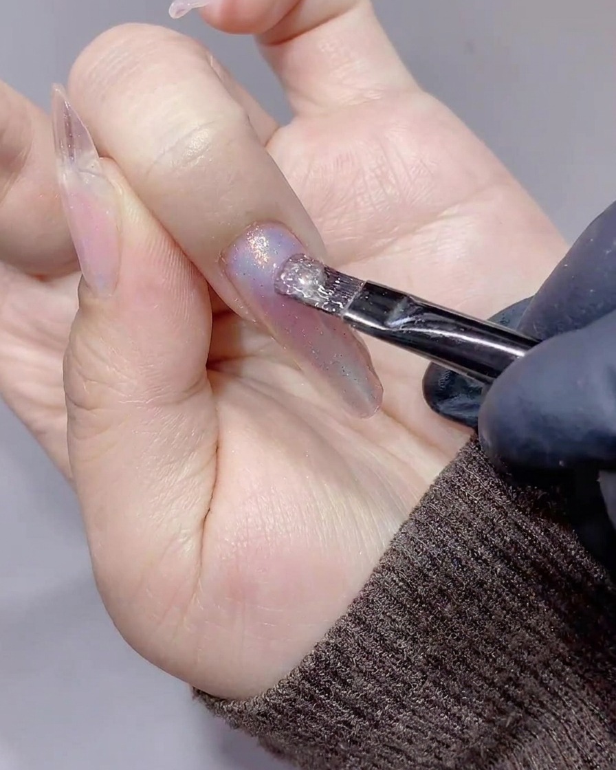 Un pennello che applica un gel cat-eye trasparente e scintillante su ununghia decorata.
