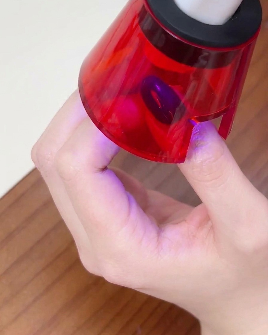 Una mano posizionata allinterno di una piccola lampada UV per unghie, con il dito centrato per polimerizzare lo smalto.