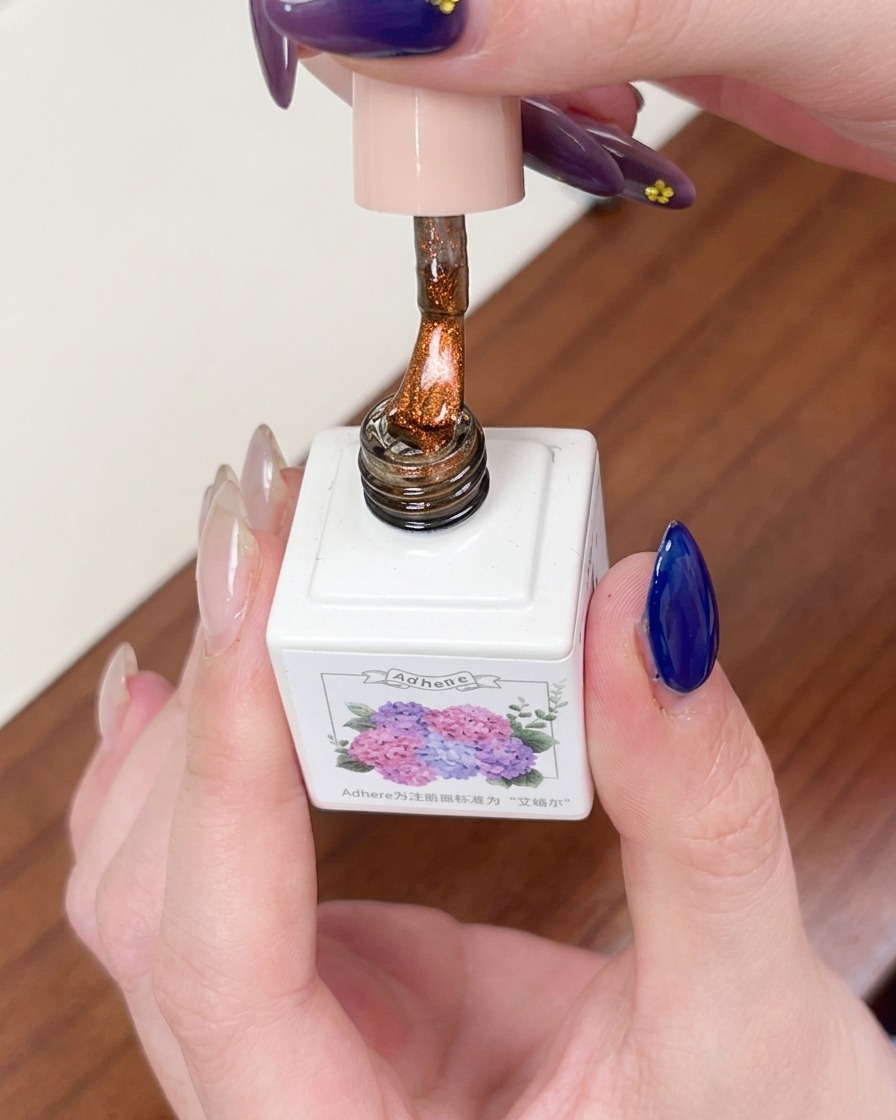 Un pennello che applica uno strato di gel magnetico cat eye color ambra trasparente sopra la base blu scuro.