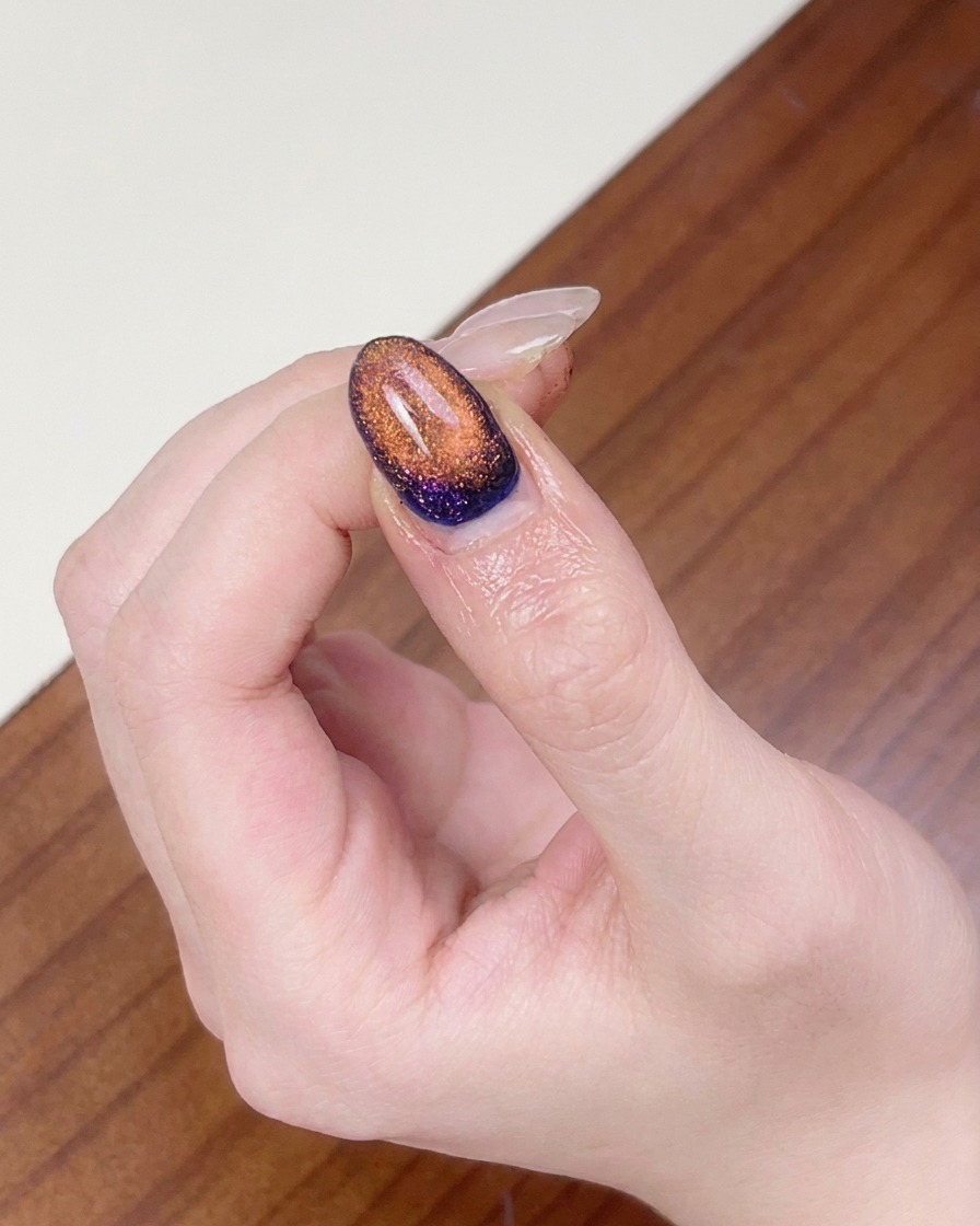 Un dito posizionato sotto una lampada UV per unghie per polimerizzare la nail art cat eye magnetica completata.