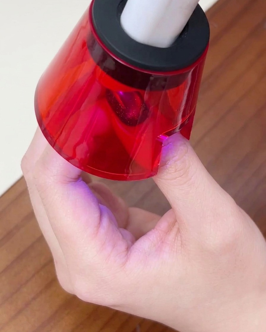 Il dito di una persona appoggiato sotto una piccola lampada UV/LED rossa per unghie per polimerizzare lo strato finale di gel.