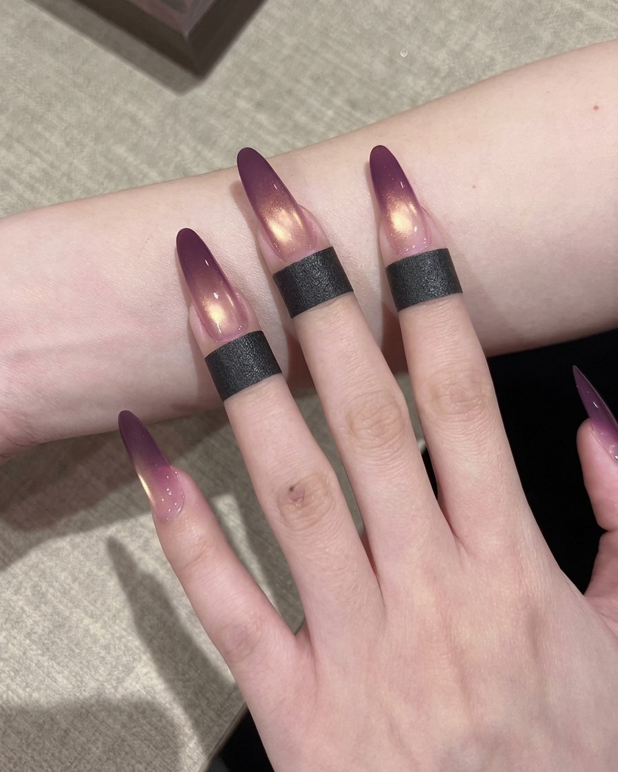 Un pennellino che applica uno strato di smalto gel cat-eye dorato e scintillante su ununghia che ha già una sfumatura ombré viola.