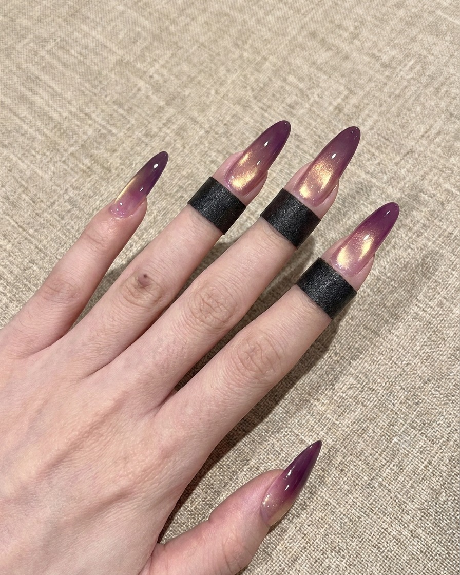 Primo piano di un pennellino che applica un top coat trasparente e lucido su ununghia cat-eye sfumata viola e oro.