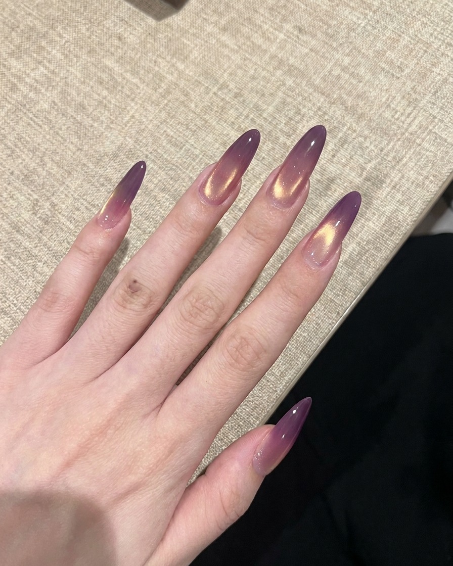 Una mano con unghie cat-eye finite con sfumatura viola e oro che viene polimerizzata sotto una lampada UV per unghie.