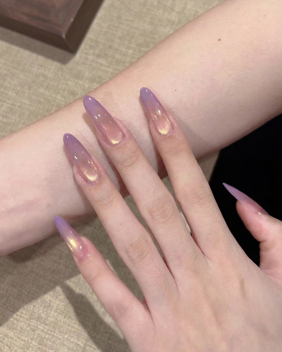 Primo piano di un pennello piatto che deposita una piccola goccia di gel viola traslucido sulla punta di ununghia stiletto trasparente.