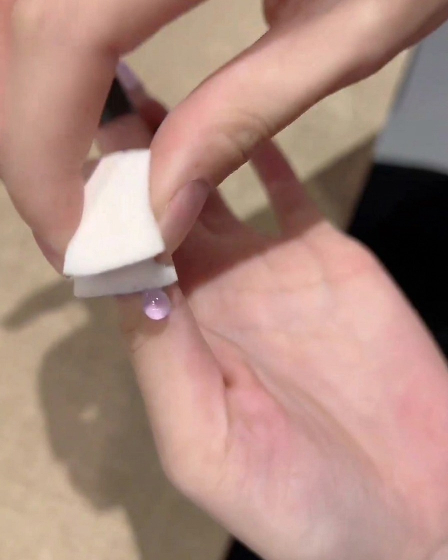 Una mano usa una piccola spugnetta bianca per tamponare e sfumare il gel viola dalla punta verso il centro dellunghia.