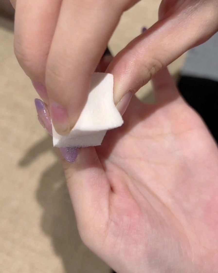 Primo piano della spugnetta che tampona ripetutamente il bordo del gel viola per perfezionare la sfumatura.