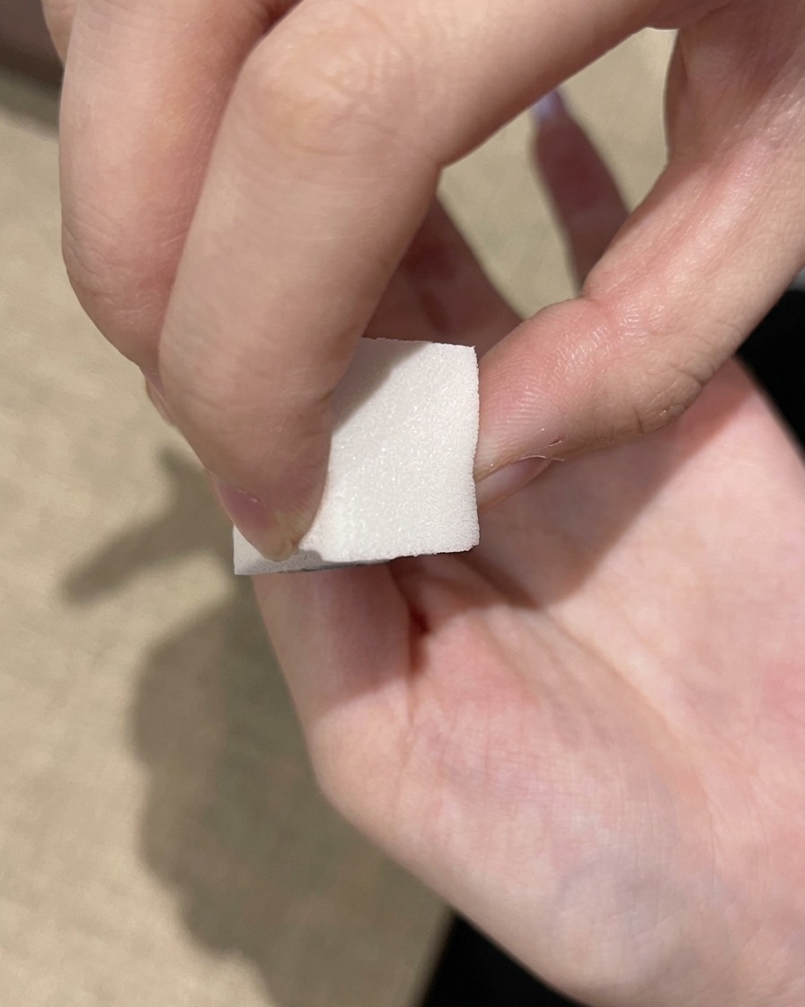 Una spugnetta per trucco bianca tampona un gel viola intenso sulla punta di ununghia.