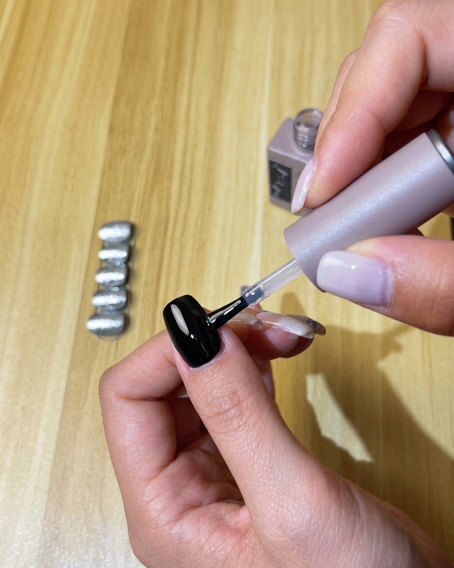Applicazione di uno strato trasparente di top coat no-wipe sullunghia in gel nera polimerizzata.
