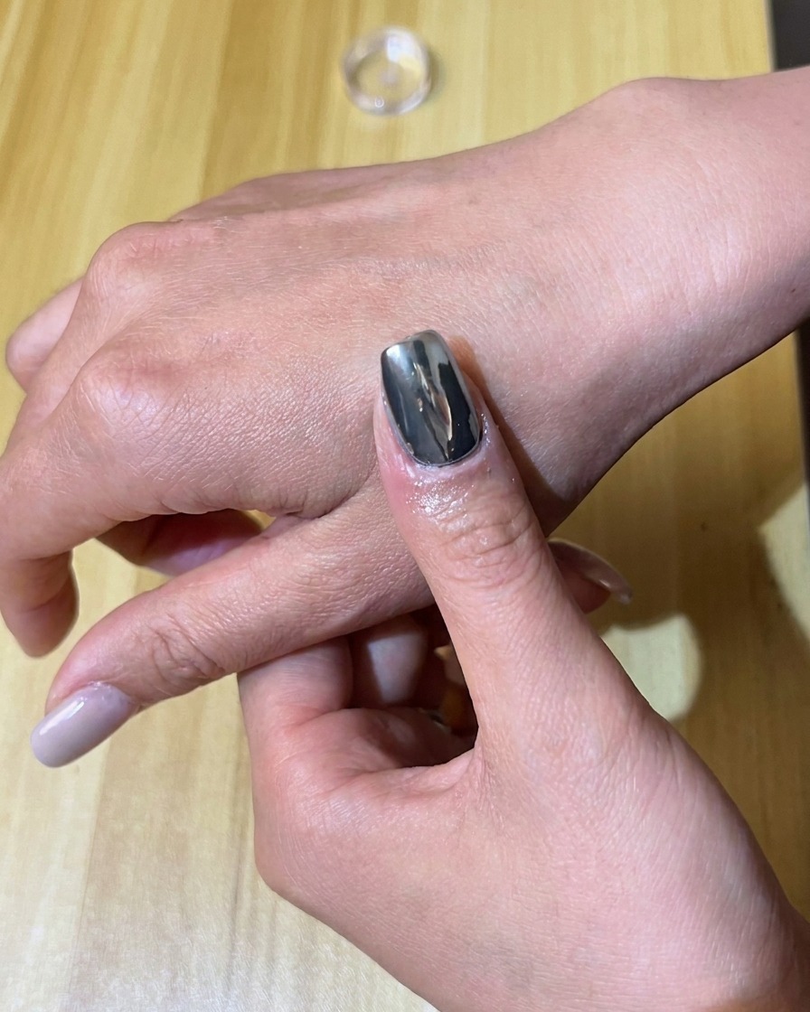 Un applicatore in spugna sfrega il pigmento cromo argento su ununghia smaltata con gel nero.