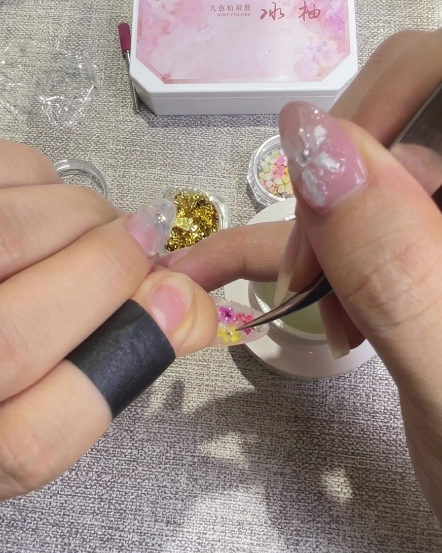 Delle pinzette riposizionano delicatamente un petalo di fiore secco sulla superficie dellunghia per ottenere un design equilibrato.
