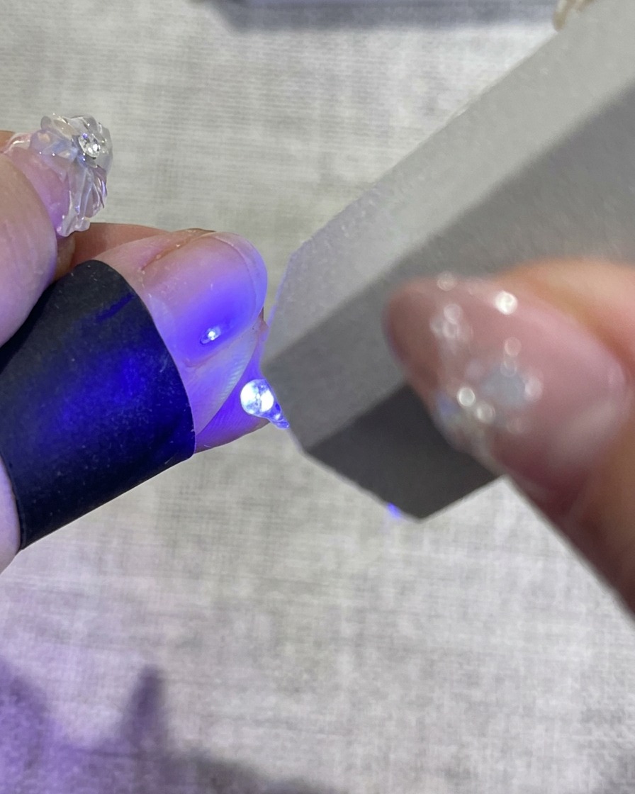 Una mano con unghie decorate a motivo floreale inserita allinterno di una lampada per unghie UV, con la luce blu emessa dalla macchina per polimerizzare lo smalto.